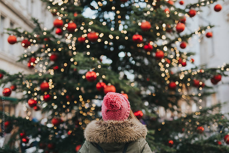 Girl with green parka and pink beanie standing in front of a christmas tree