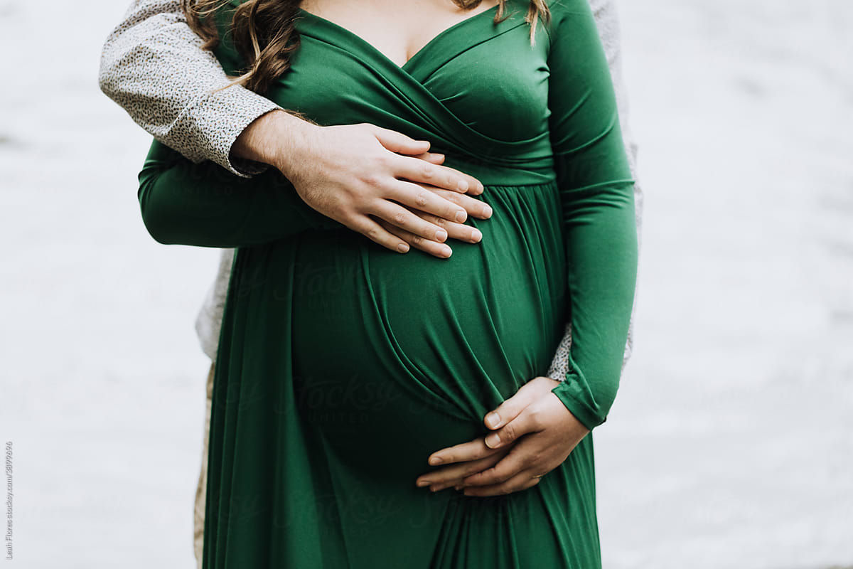 A Couple Standing in front of a River Hug a Pregnant Belly