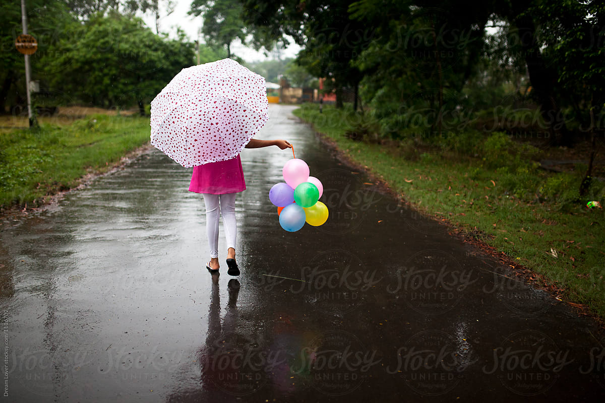 Teenage girl walking through a rain wet road with colorful balloons