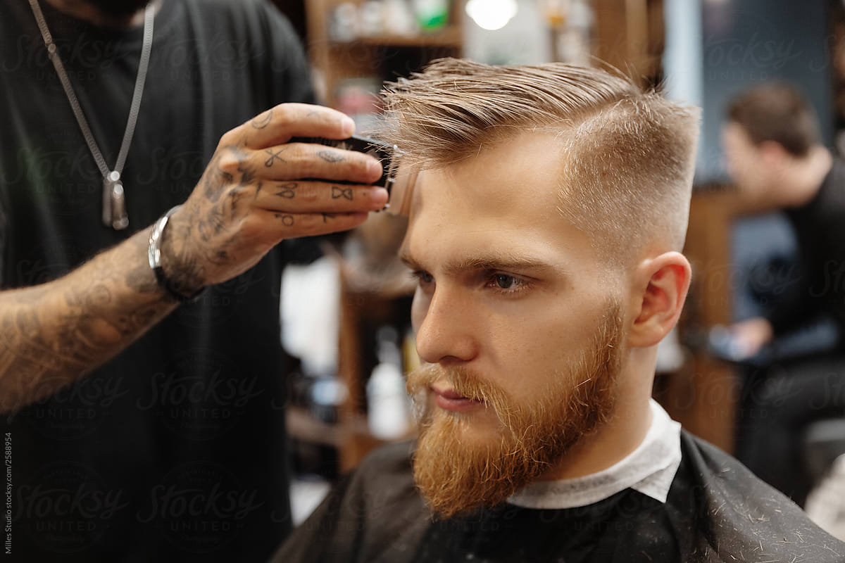Crop barber trimming hair of bearded man
