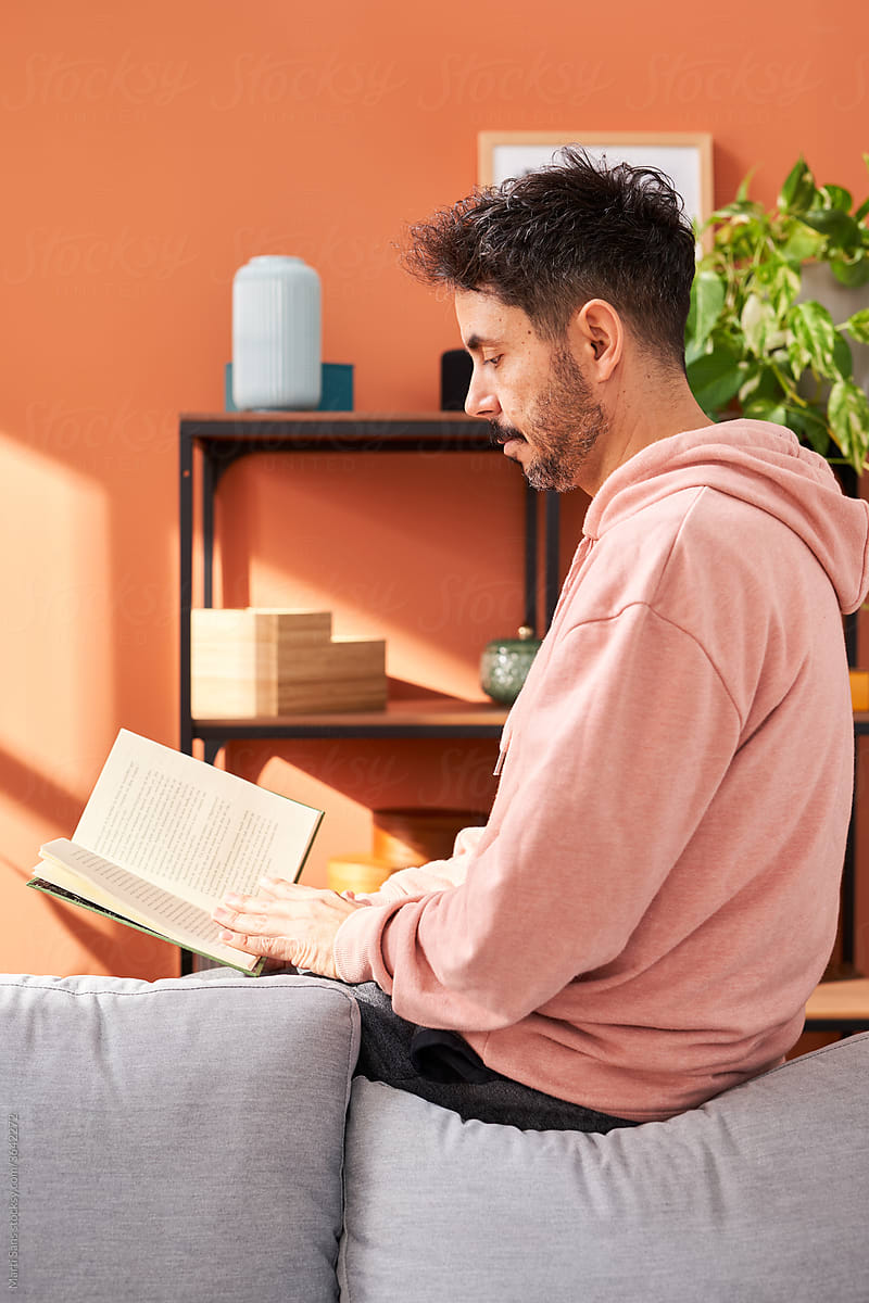 Adult man sitting on sofa and reading book