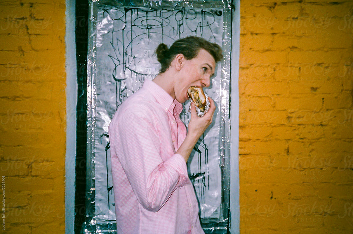 Man start to eat a burger outside the diner in front of a yellow wall