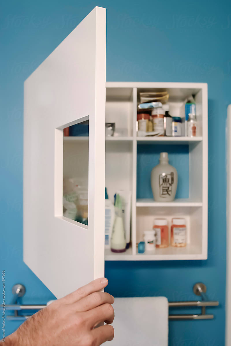 Hand opening Medicine Cabinet in bathroom of home with medication