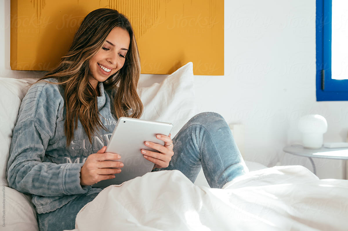 Happy woman using tablet in bedroom
