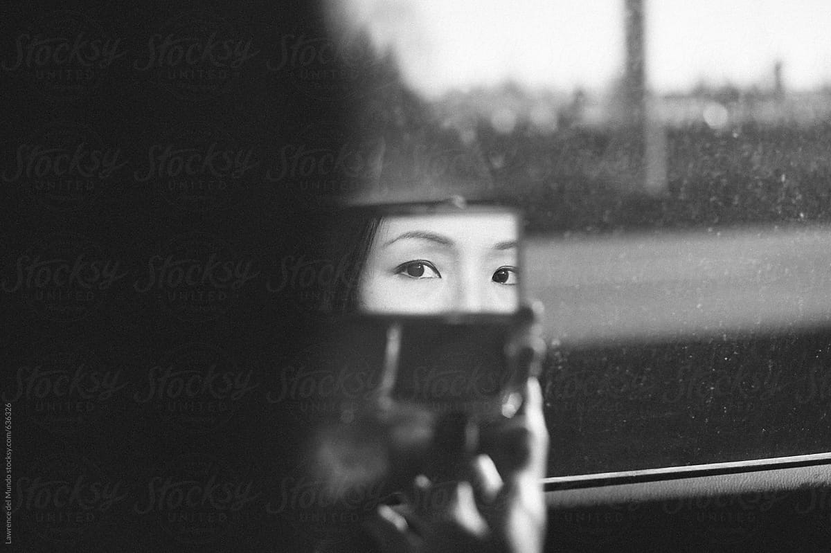 Attractive woman looks at mirror while putting on make-up inside the car