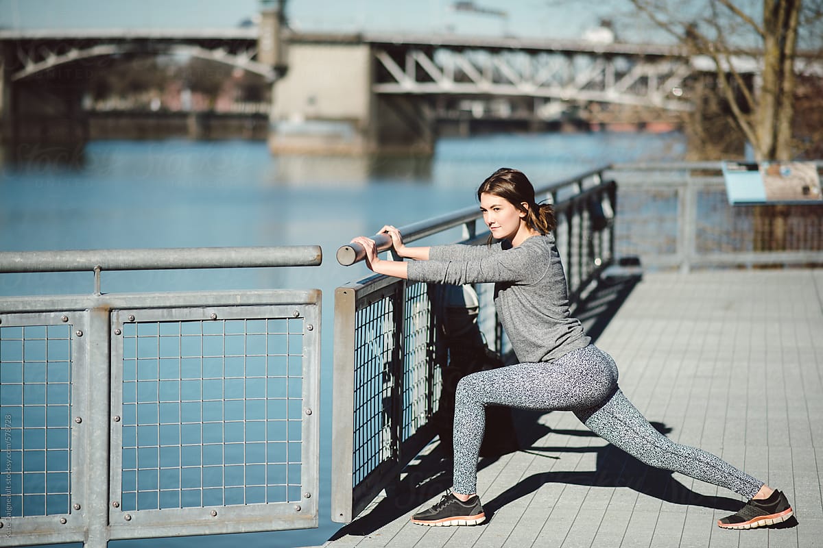 Young woman stretches before a run along a river front path in the city.