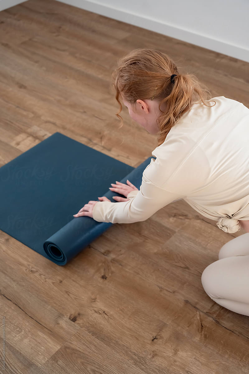 Young lady putting yoga mat on floor in studio