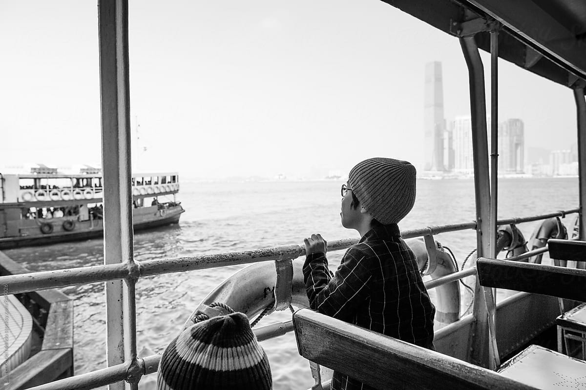 A young boy looking out into the bay  and watching other boats pass while on a ferry boat ride.