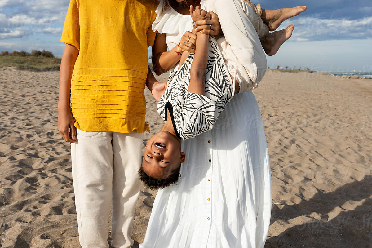Family on the beach with little kid upside down hanging