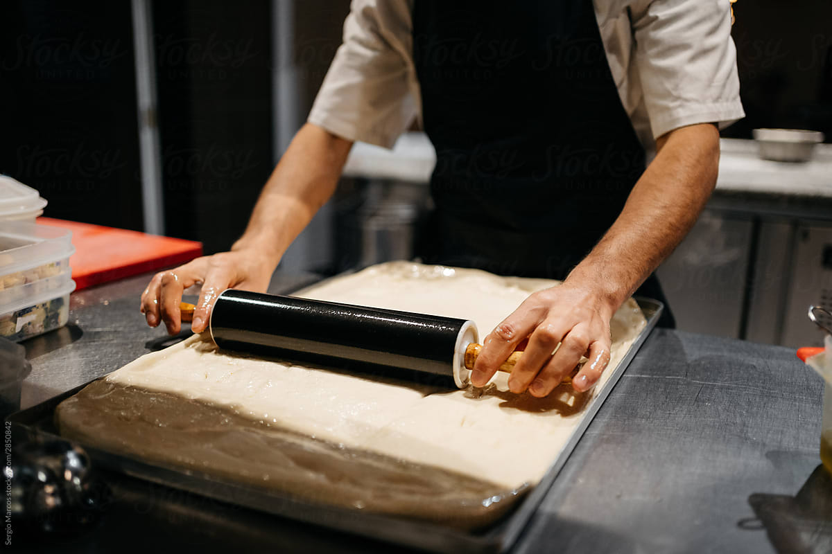 Cook preparing the pizza dough with a rolling pin