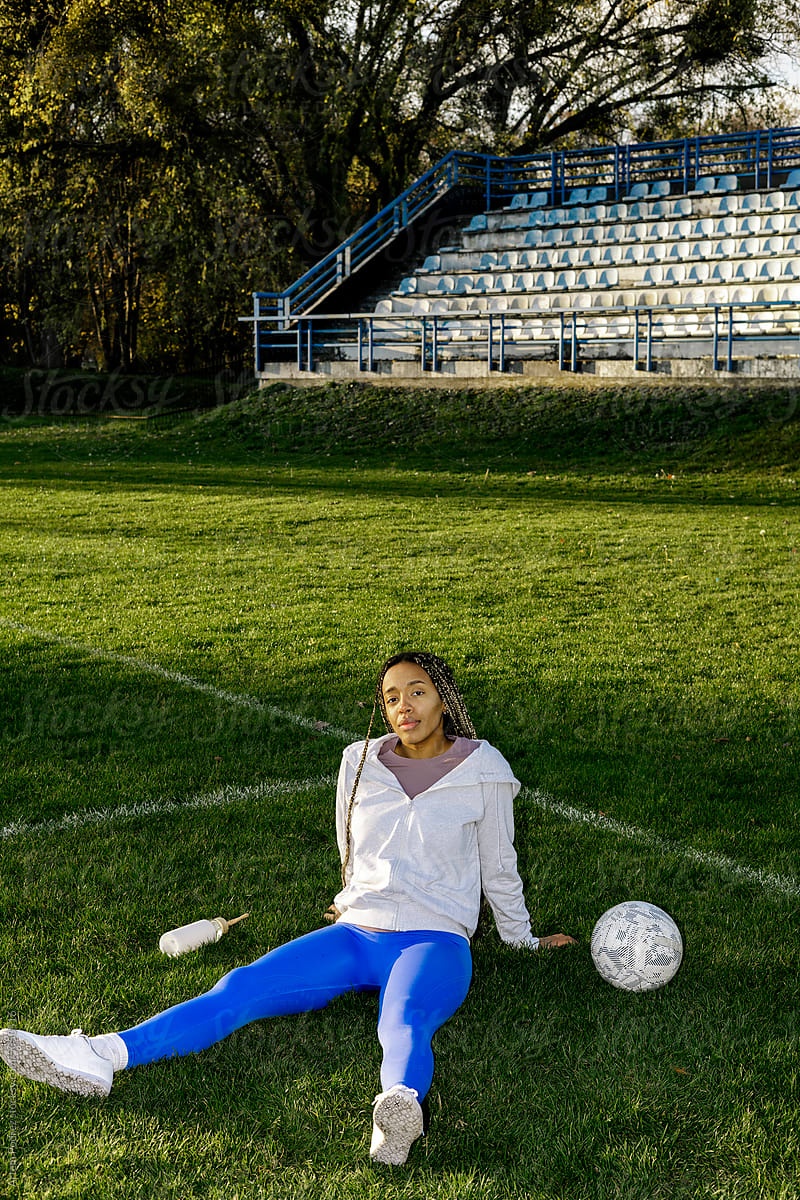 A woman in sportswear is sitting on a soccer lawn