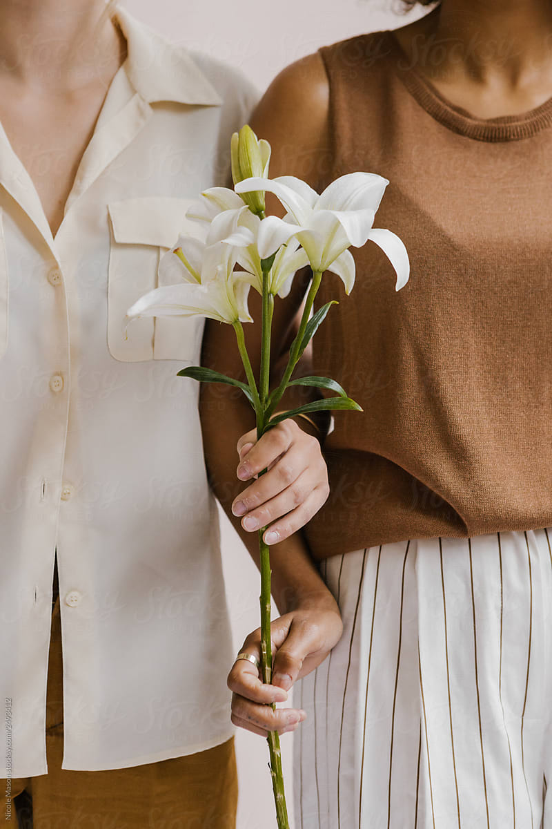 two young stylish women posing together holding florals and tropical leaves