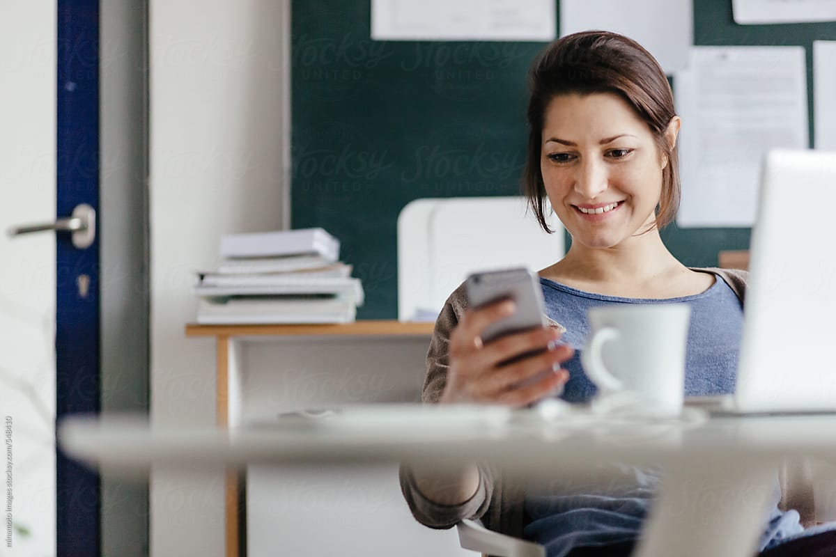 Happy Young Woman Checking Smartphone In Her Office