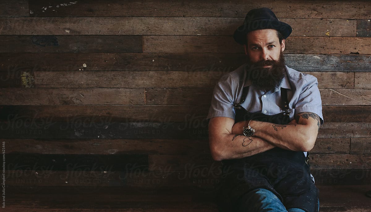 Portrait of stylish 30-something man with beard - sitting near reclaimed wood wall