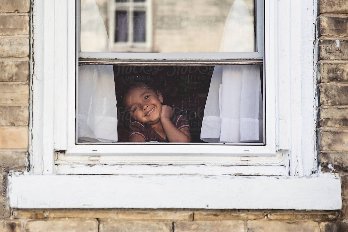 A young child sitting and smiling in front of a window