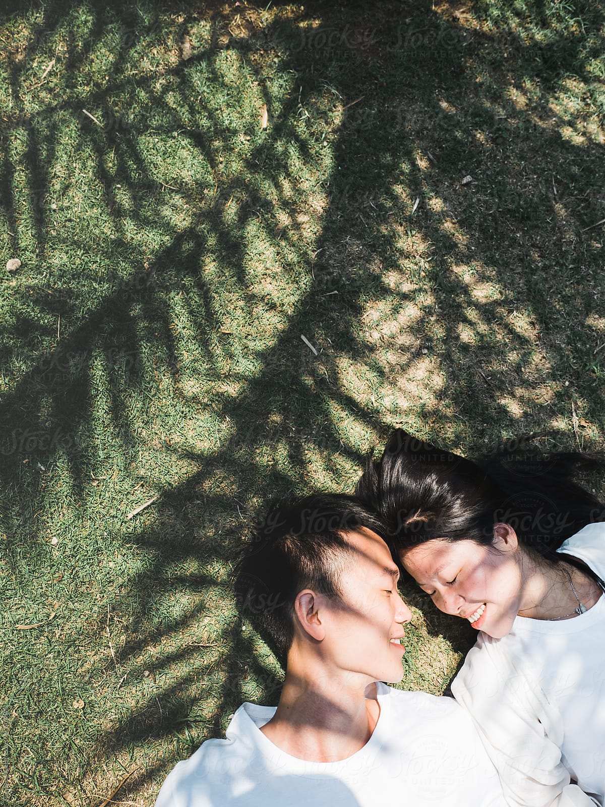 Chinese Young Couple Lying On Ground With Palm Tree Shadow By Stocksy