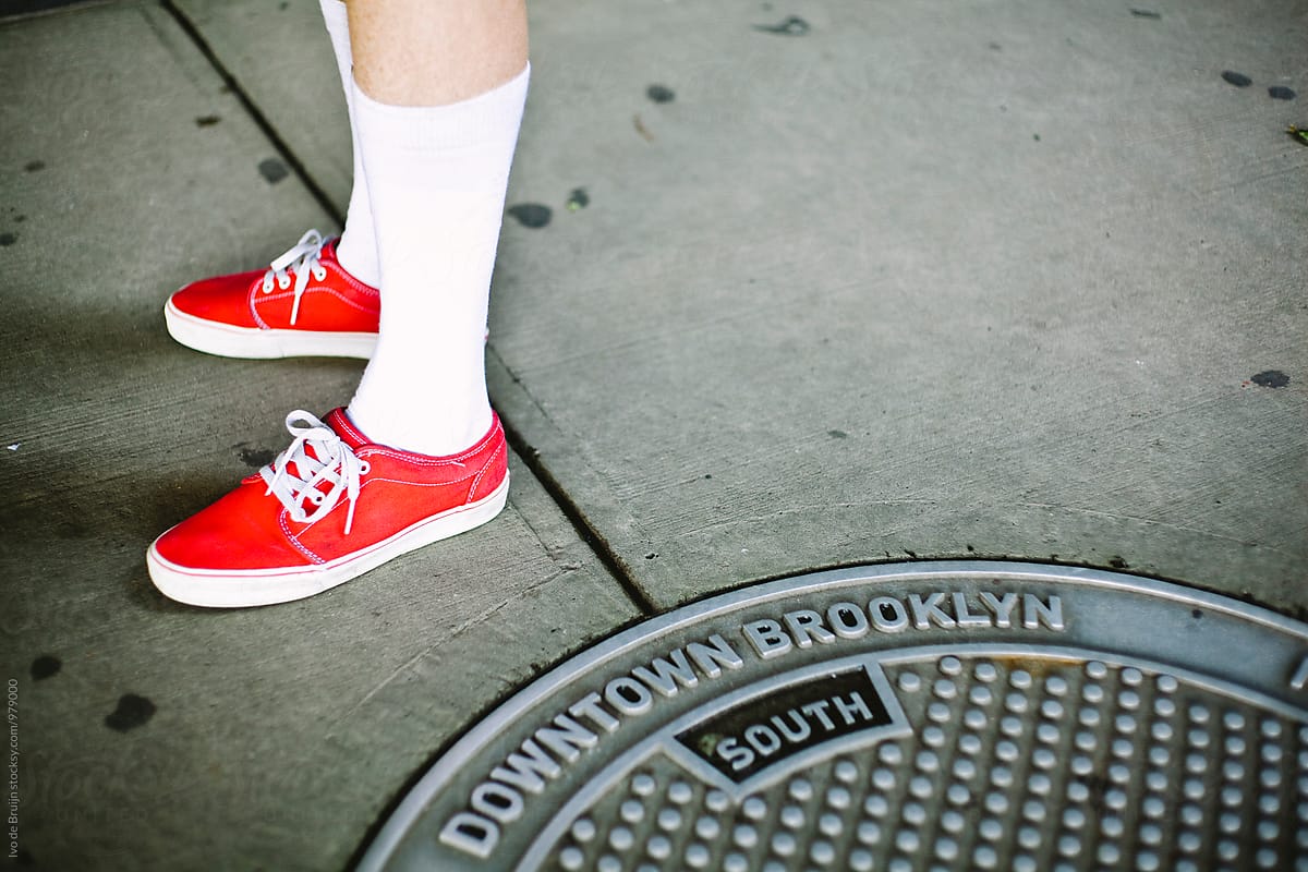 Close up of red someone's red sneakers standing next to a manhole cover in Brooklyn