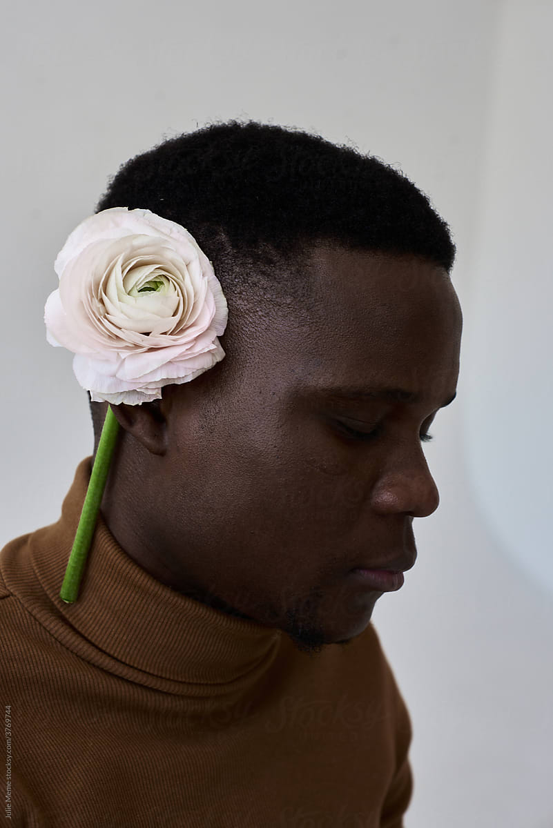 Closeup portrait of an african guy in the beige poloneck and a pale pink flower over his ear
