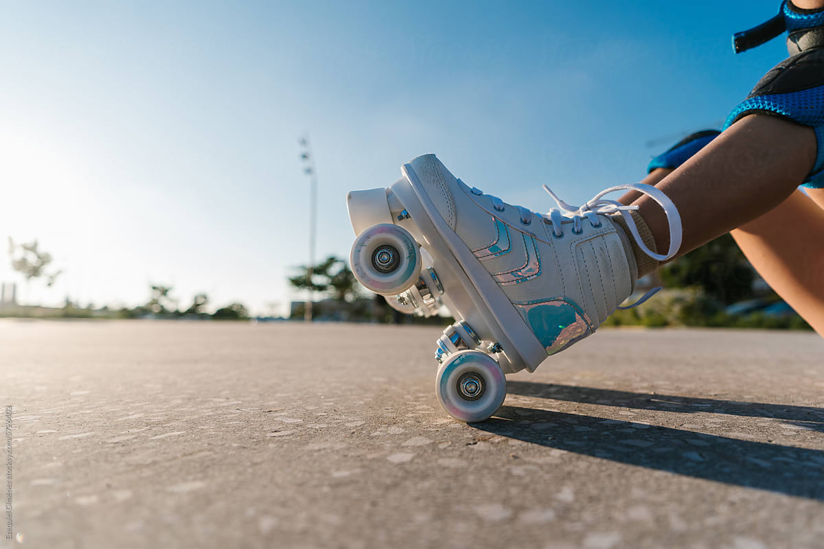 Crop girl in roller skates sitting on ground