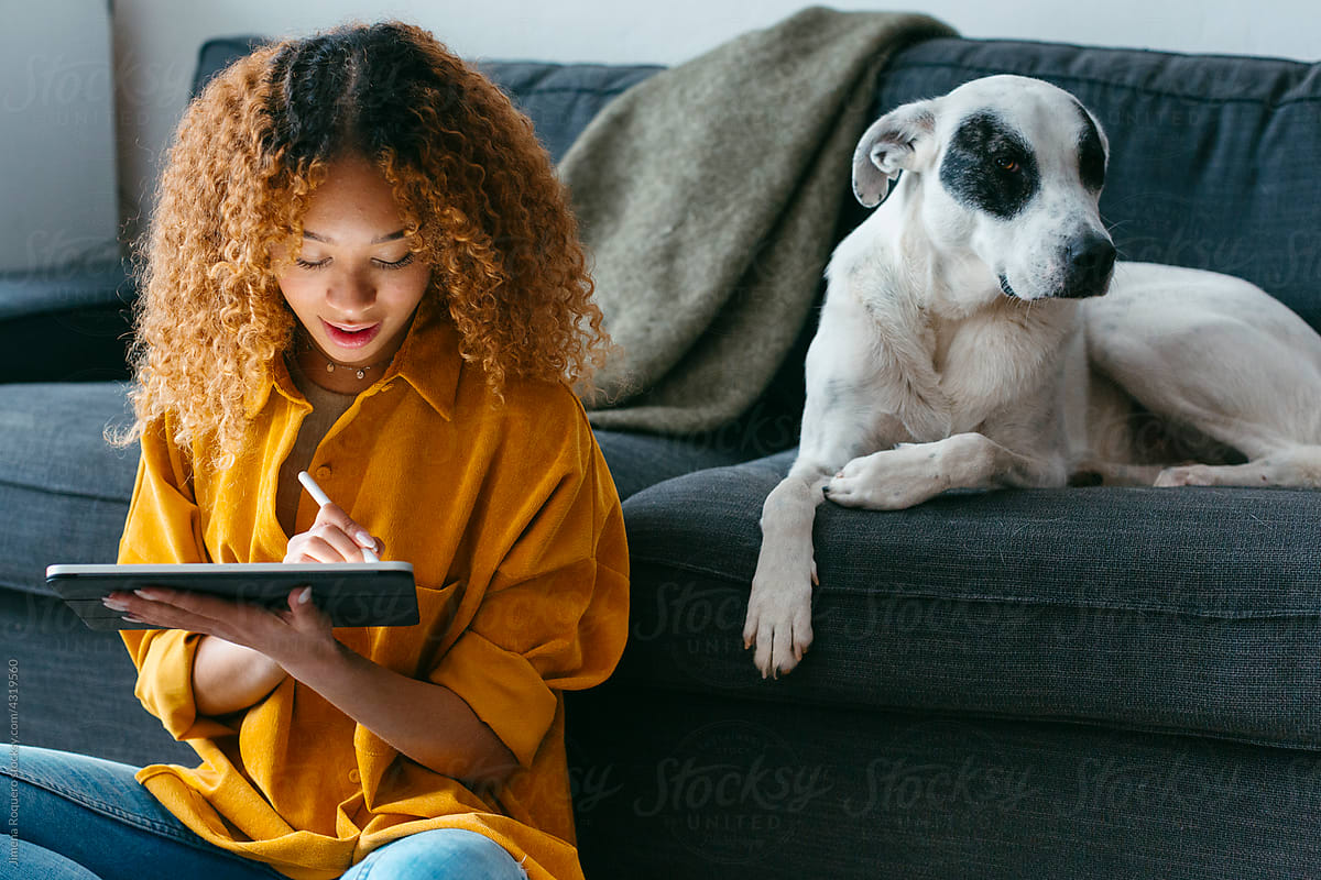 Teenager at home living room using tablet with dog