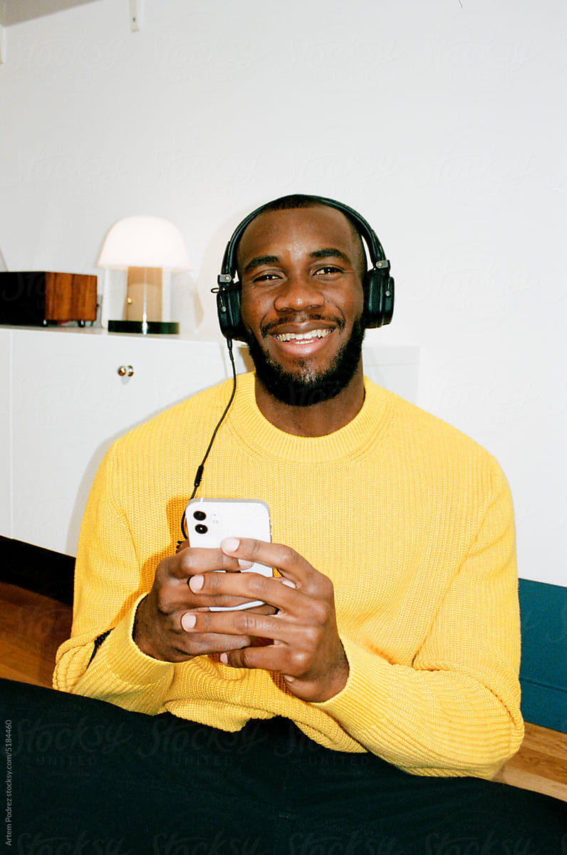 A black man in a yellow sweater listens to music with headphones