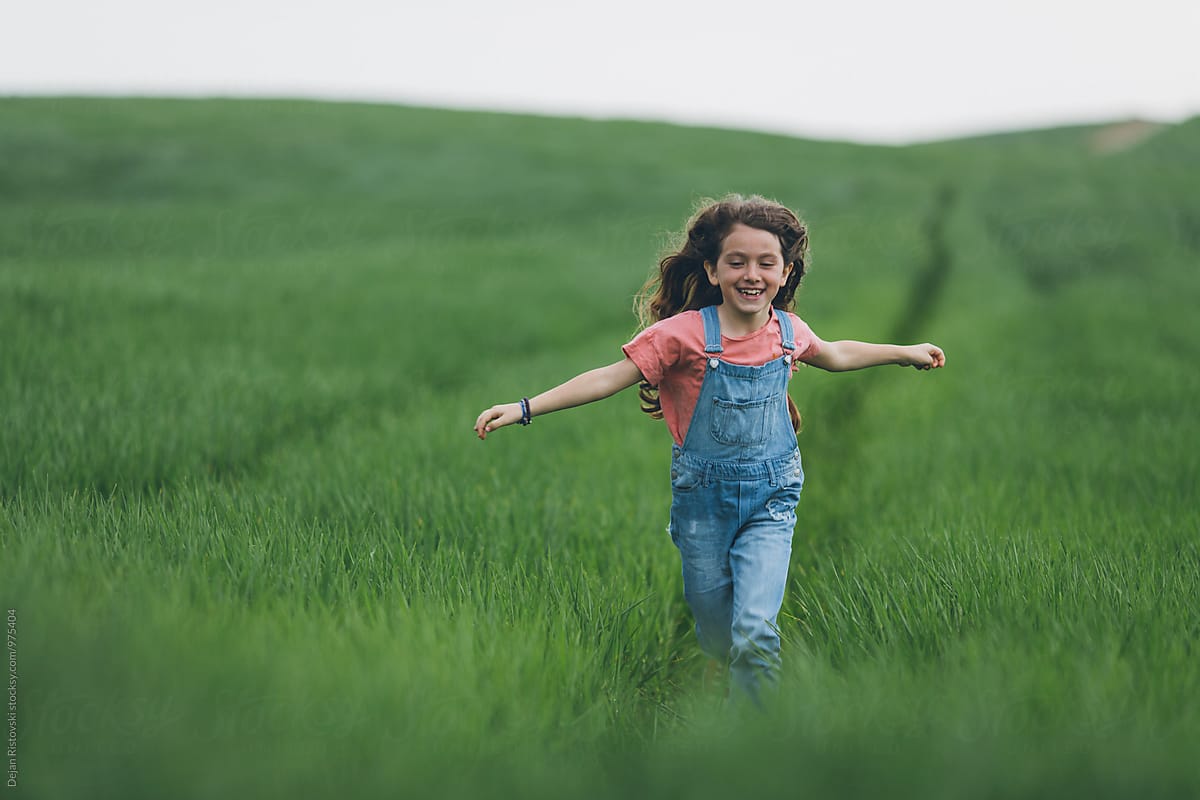 Happy little girl running along green  wreath field.