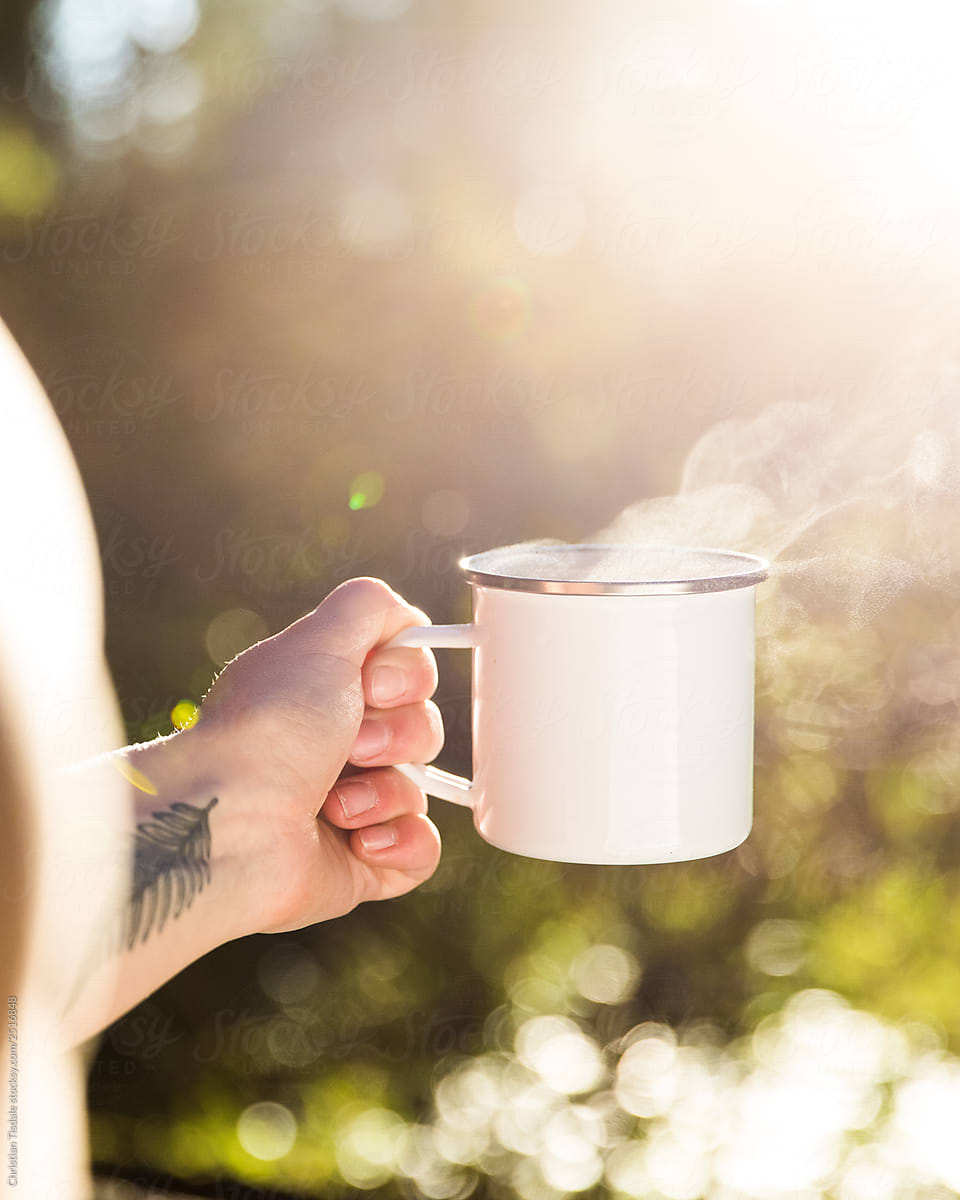 Blank white enamel coffee mug held by a hand in the forest