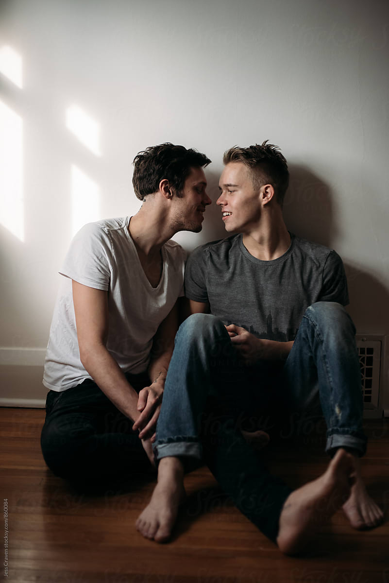 Young Gay Male Couple In Love Sitting On Bedroom Floor
