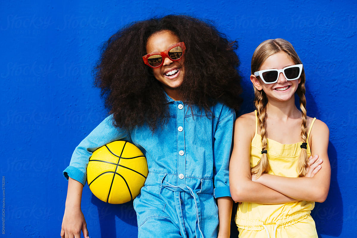 Cheerful multiethnic friends in stylish sunglasses holding ball while standing on street
