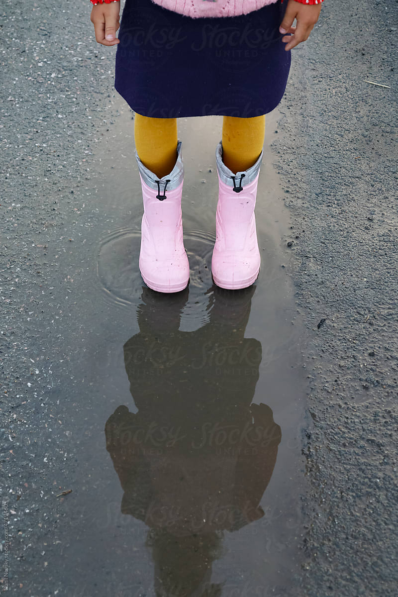 Anonymous little girl in boots standing in puddle