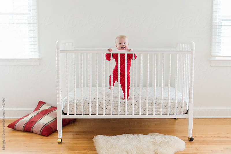 baby standing in her crib in red pajamas