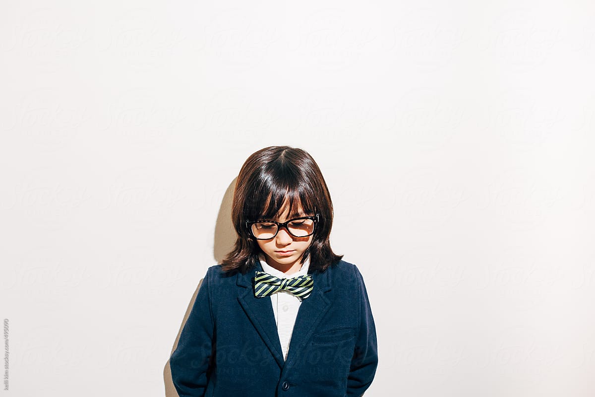 Young boy in glasses and bow tie stands alone, appearing sad