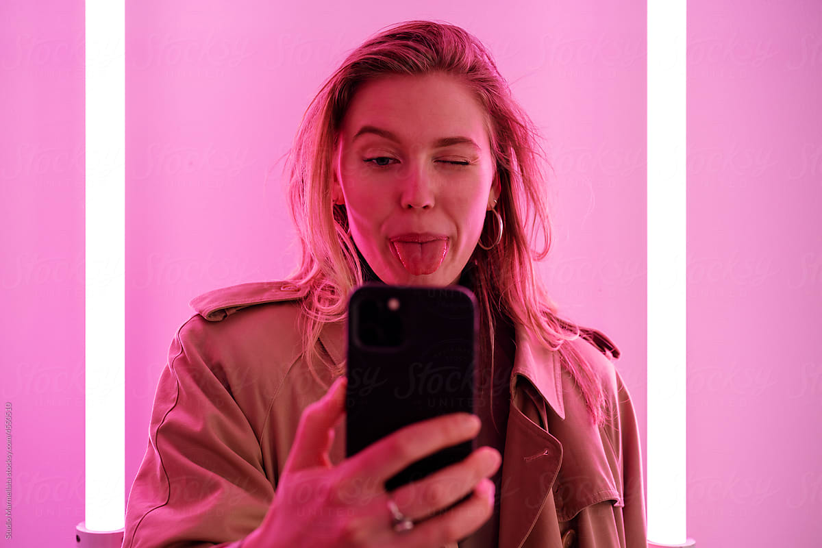 Funny woman taking selfie on smartphone in pink light
