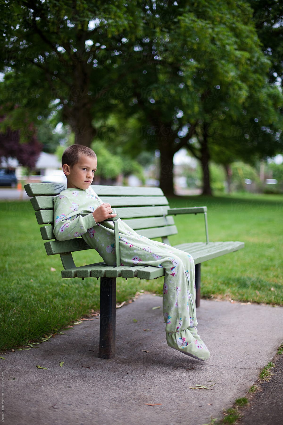Sad Boy In Pajamas Sitting Alone On Park Bench by Carleton Photography