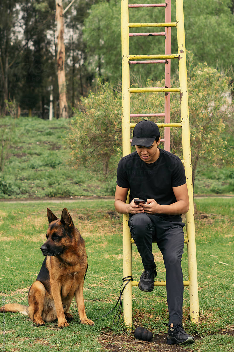 Man with his pet in the park using the cell phone.