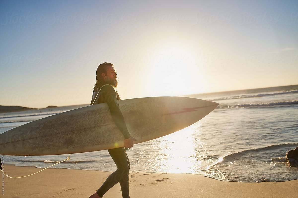 Retired Healthy Mature Surfer walking into the ocean with surfboard at sunrise