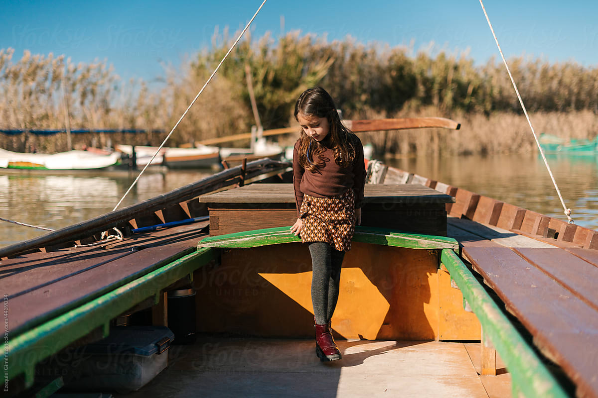 Child standing in weathered boat on pond
