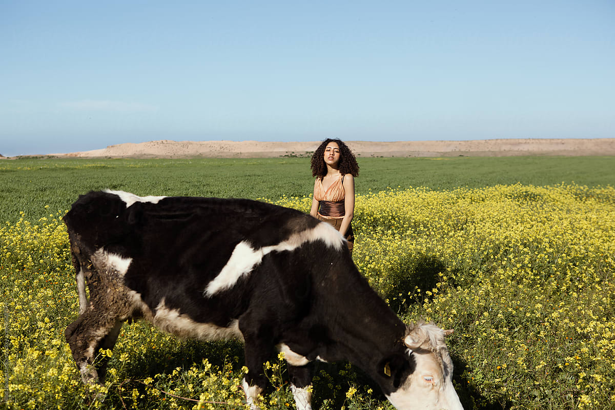 Girl with curly hair posing in a flowers field next to a cow
