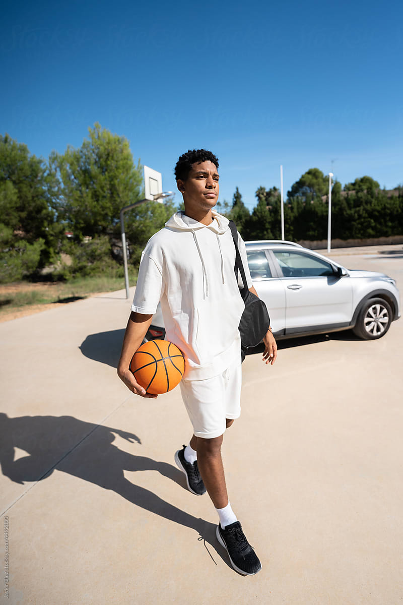 Young basketball player walking near car