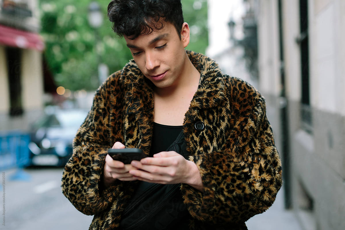 Portrait of young attractive gay man walking in the streets texting on is smartphone