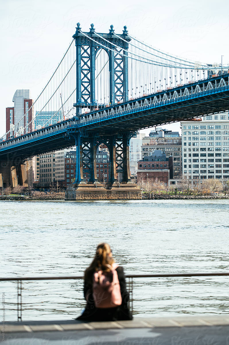 Anonymous woman admiring city near river and bridge