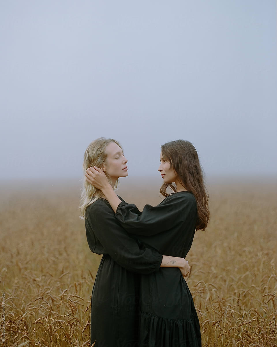 two girls in a black dress posing in a field among wheat ears