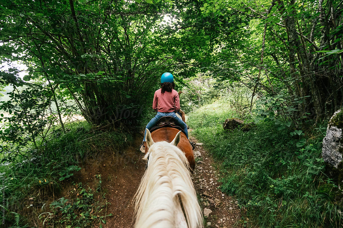 Back view, Woman riding a horse in a rural trail.