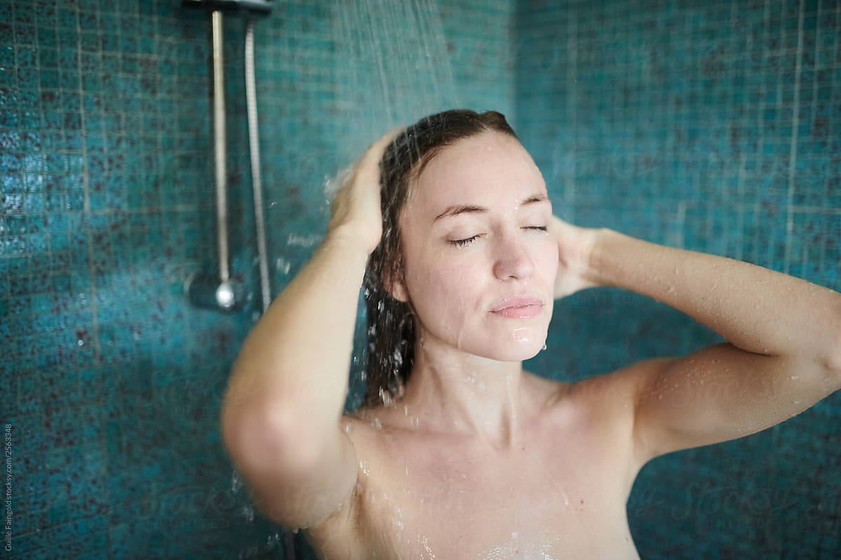 Naked brunette woman taking shower with closed eyes.