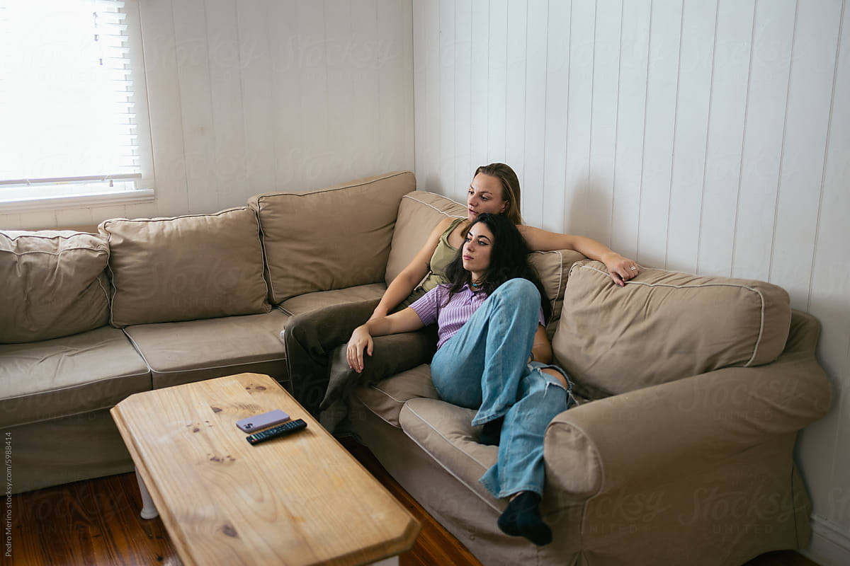 Female couple cuddling and watching TV on the couch