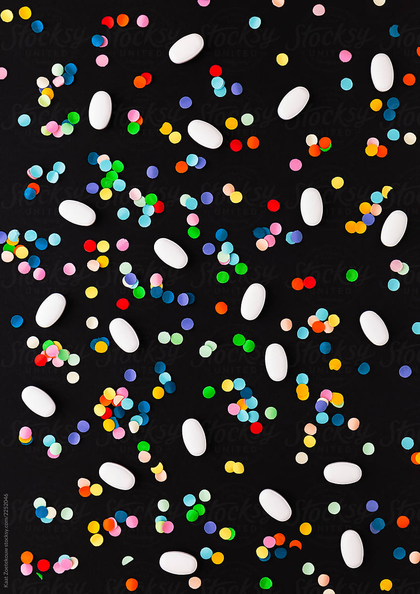 Pills and confetti scattered on a black background