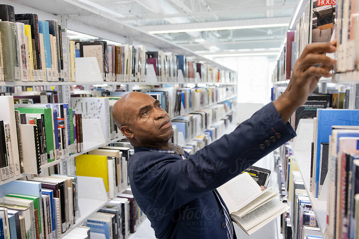 Man reaching for book on library bookshelf.