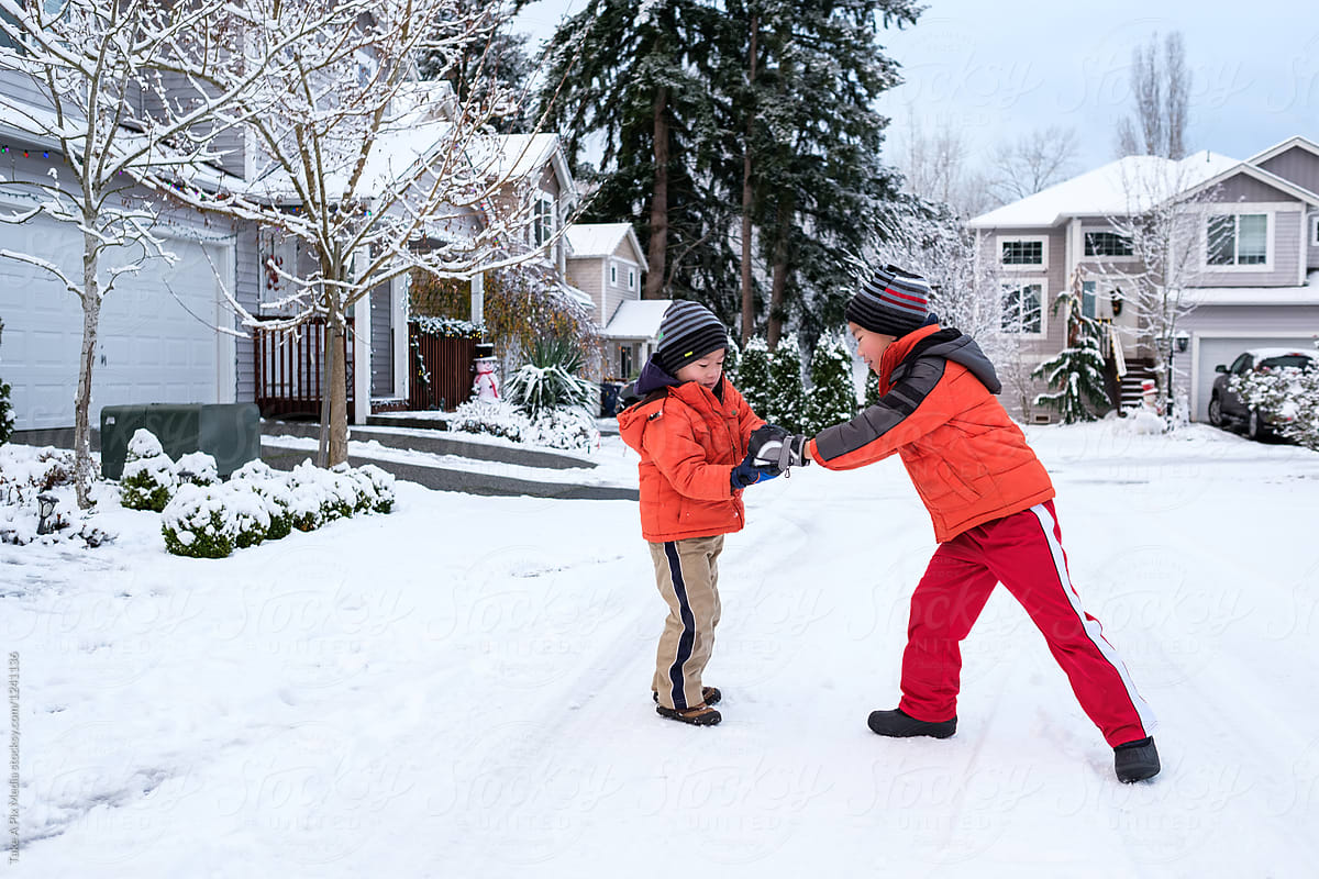 Two Asian kids playing snowball fight outside their home