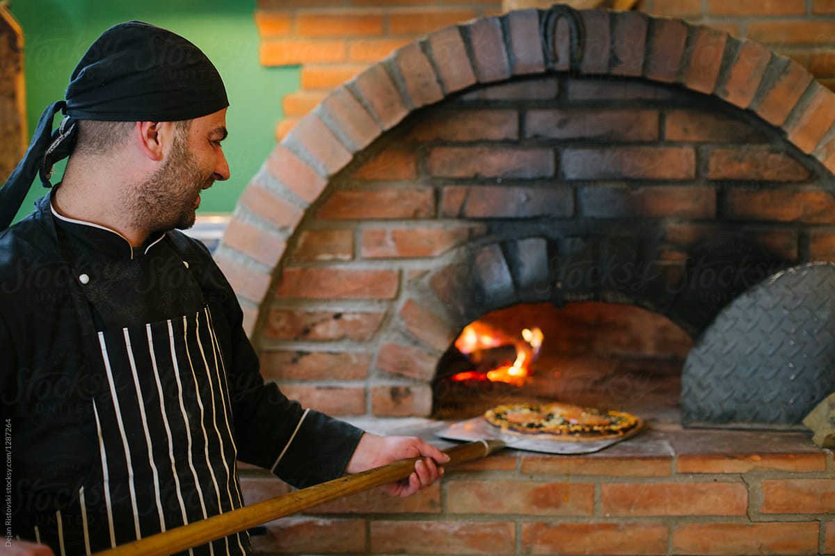 Chef putting pizza in hot rustic oven.