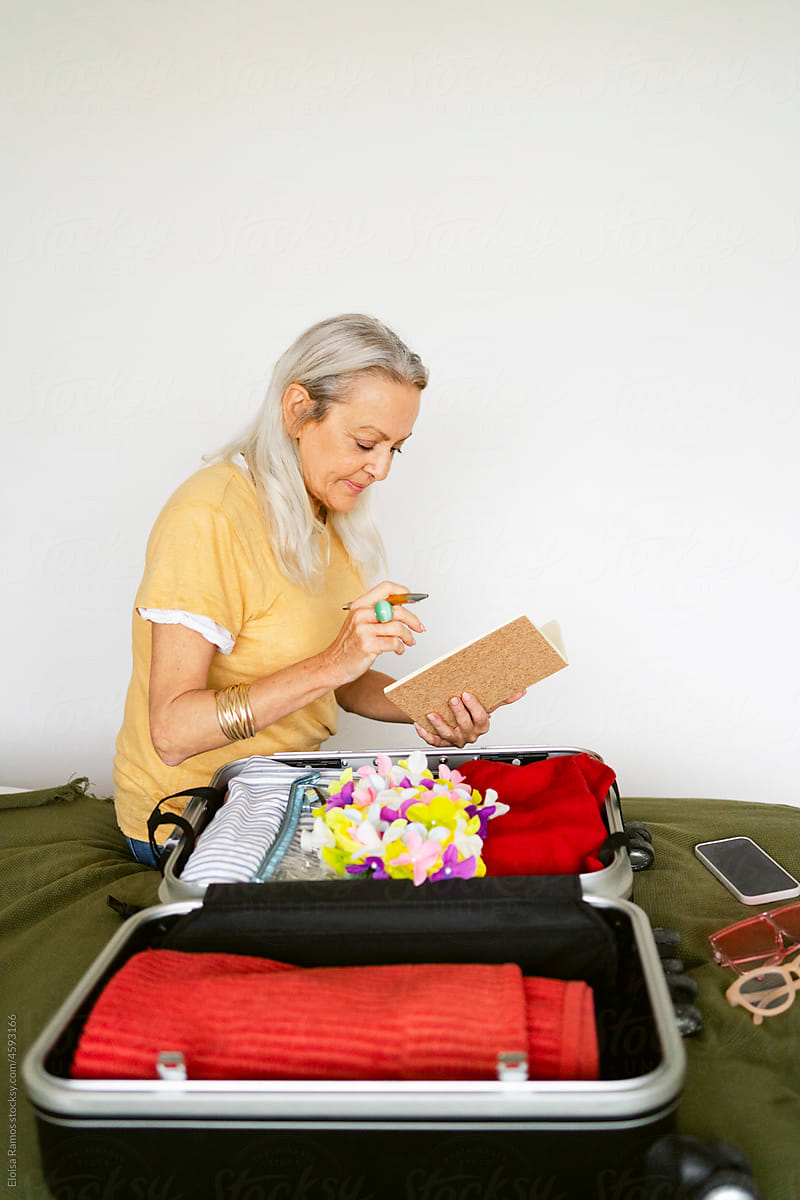 Grey-haired woman checking list by travel suitcase